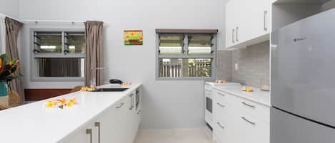 Una cocina moderna con armarios blancos, un refrigerador de acero inoxidable y una ventana con cortinas.