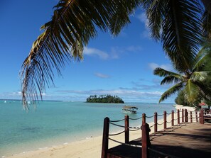 A beach with a wooden walkway, palm trees, and a boat in the water.