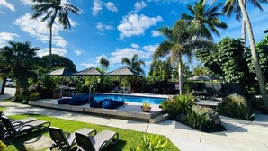 A pool area with lounge chairs, umbrellas, and palm trees. - Muri Beachcomber (Rarotonga)