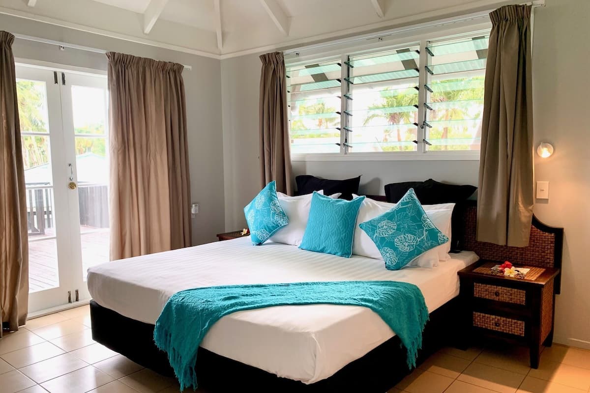 Un dormitorio con una cama grande, dos mesitas de noche, una ventana con cortinas y vistas al exterior.