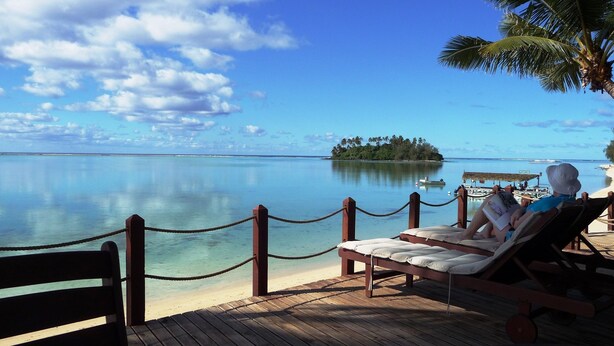 A wooden deck with lounge chairs and a rope barrier overlooking a calm sea and a small island with palm trees. - Muri Beachcomber (Rarotonga)