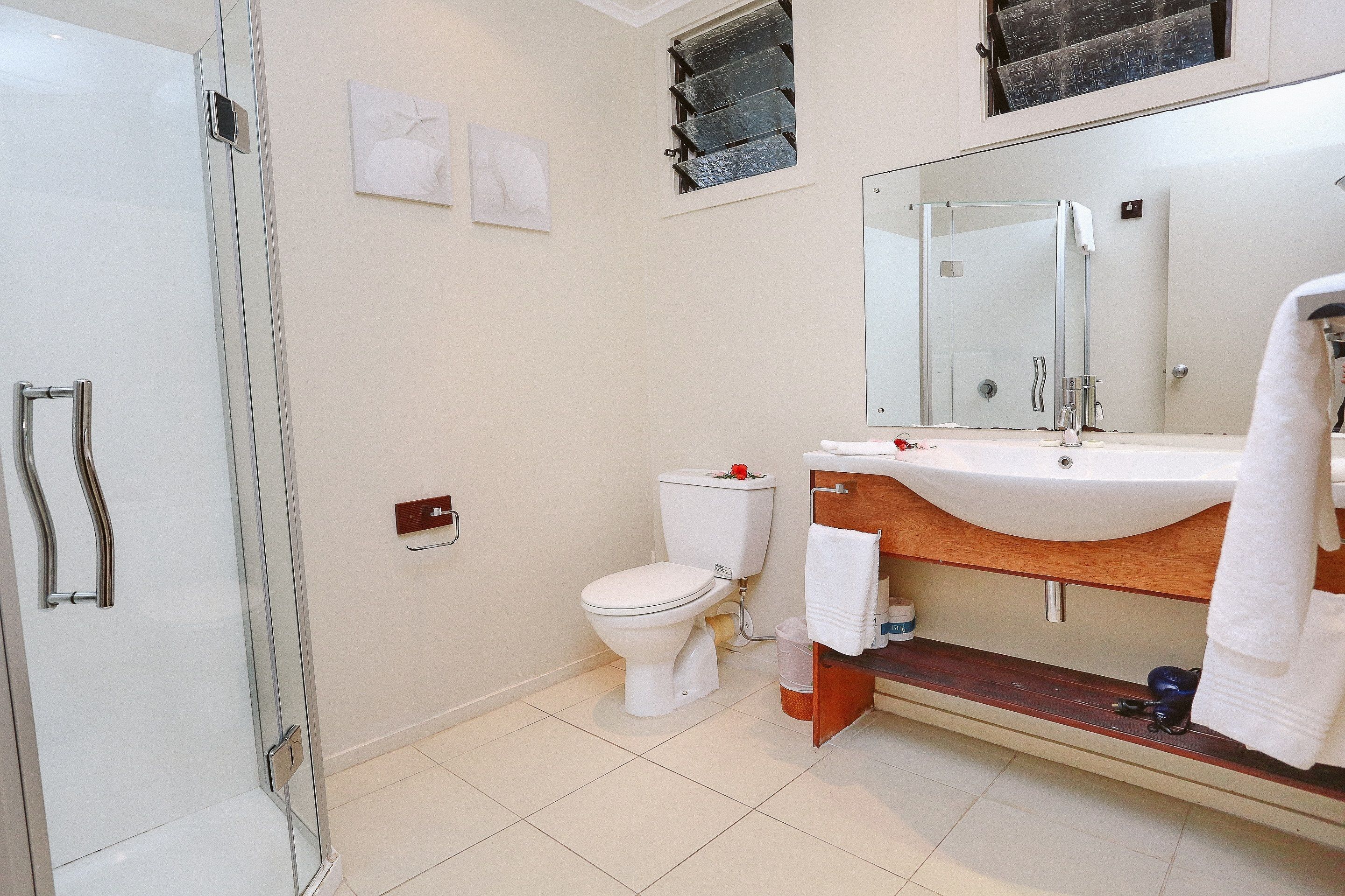 Un baño moderno con cabina de ducha de vidrio, inodoro blanco y tocador de madera con un espejo grande.