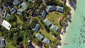 An aerial view of a coastal resort with multiple buildings, a beach, and clear turquoise waters. - Muri Beachcomber (Rarotonga)