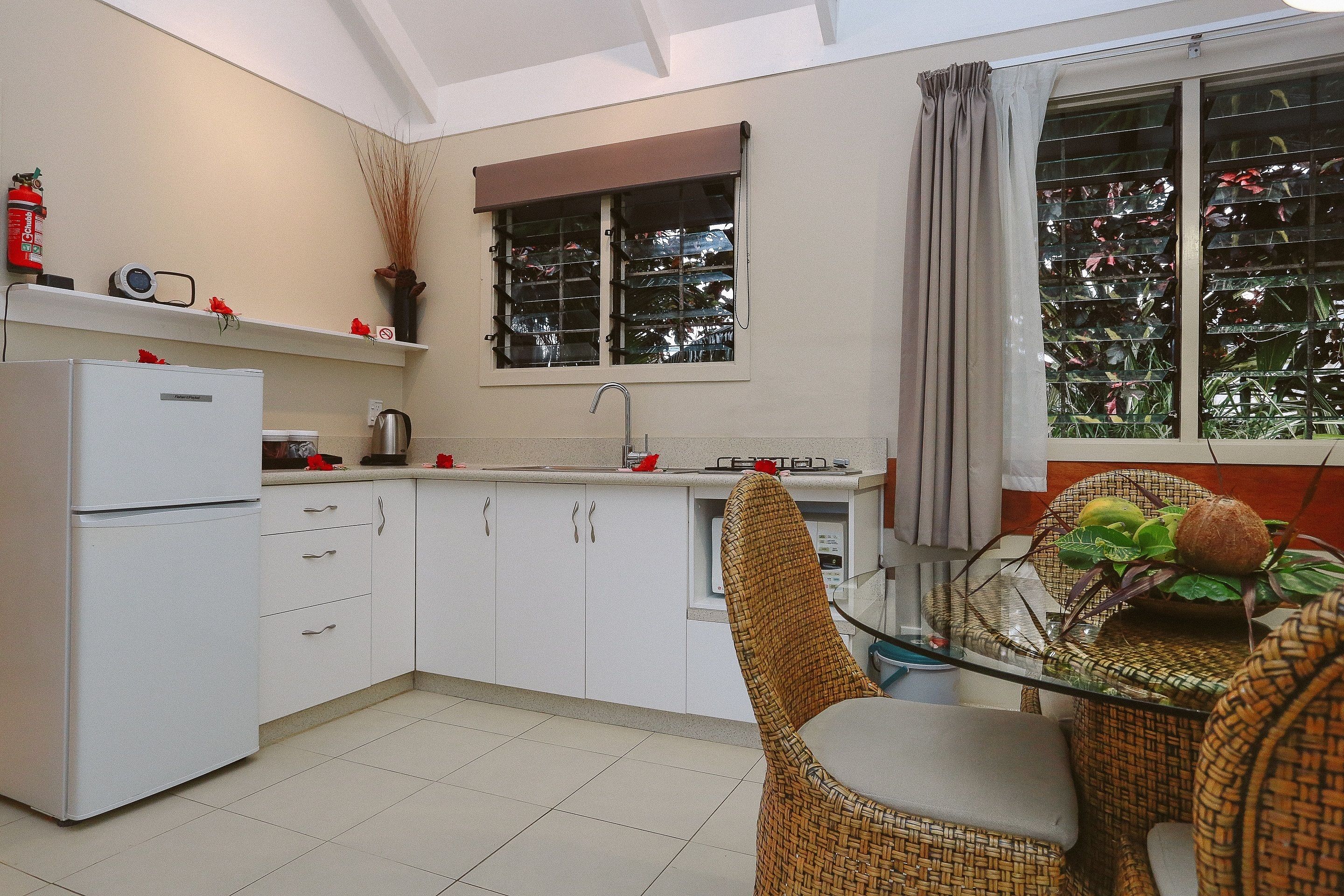 A compact kitchen with white cabinets, a white refrigerator, a sink, and a window with a curtain.