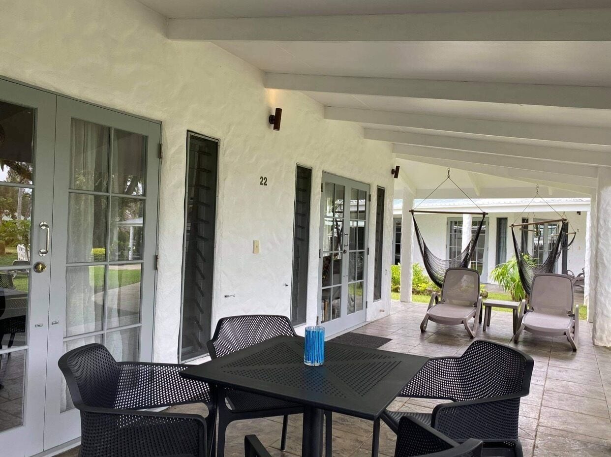 A covered patio area with a table and chairs, a hanging hammock, and a door with a number.