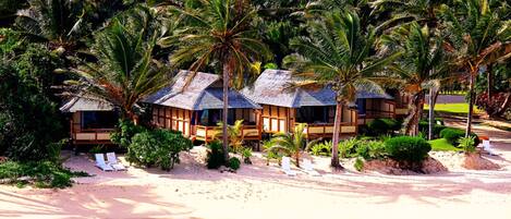 A beachfront resort with overwater bungalows, palm trees, and a clear blue sea.