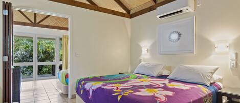 Una camera da letto con un letto grande, un ventilatore a soffitto, un condizionatore d'aria e vista su un giardino attraverso una porta in vetro.