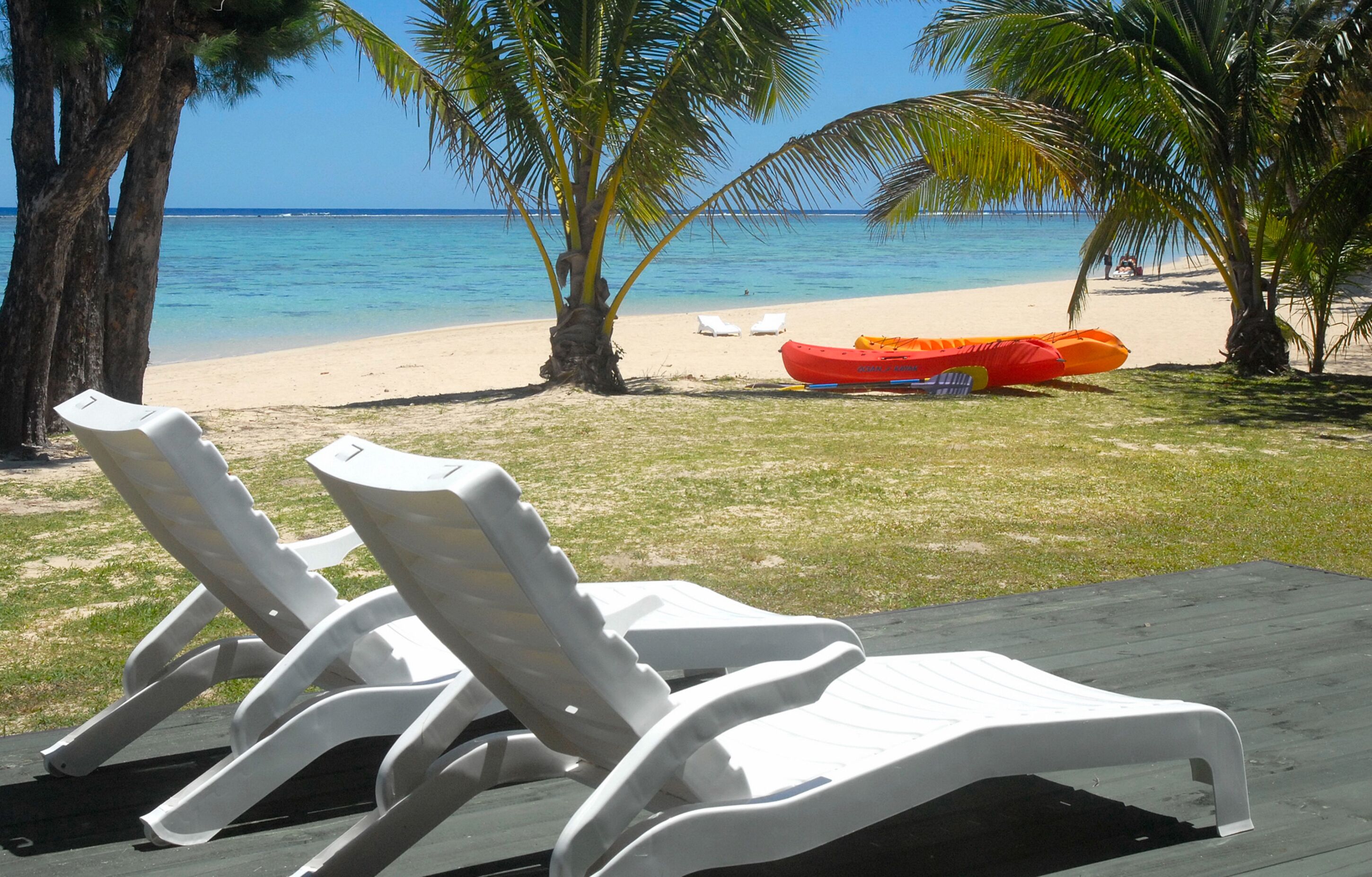 A beach view with white lounge chairs, a red inflatable boat, and palm trees.