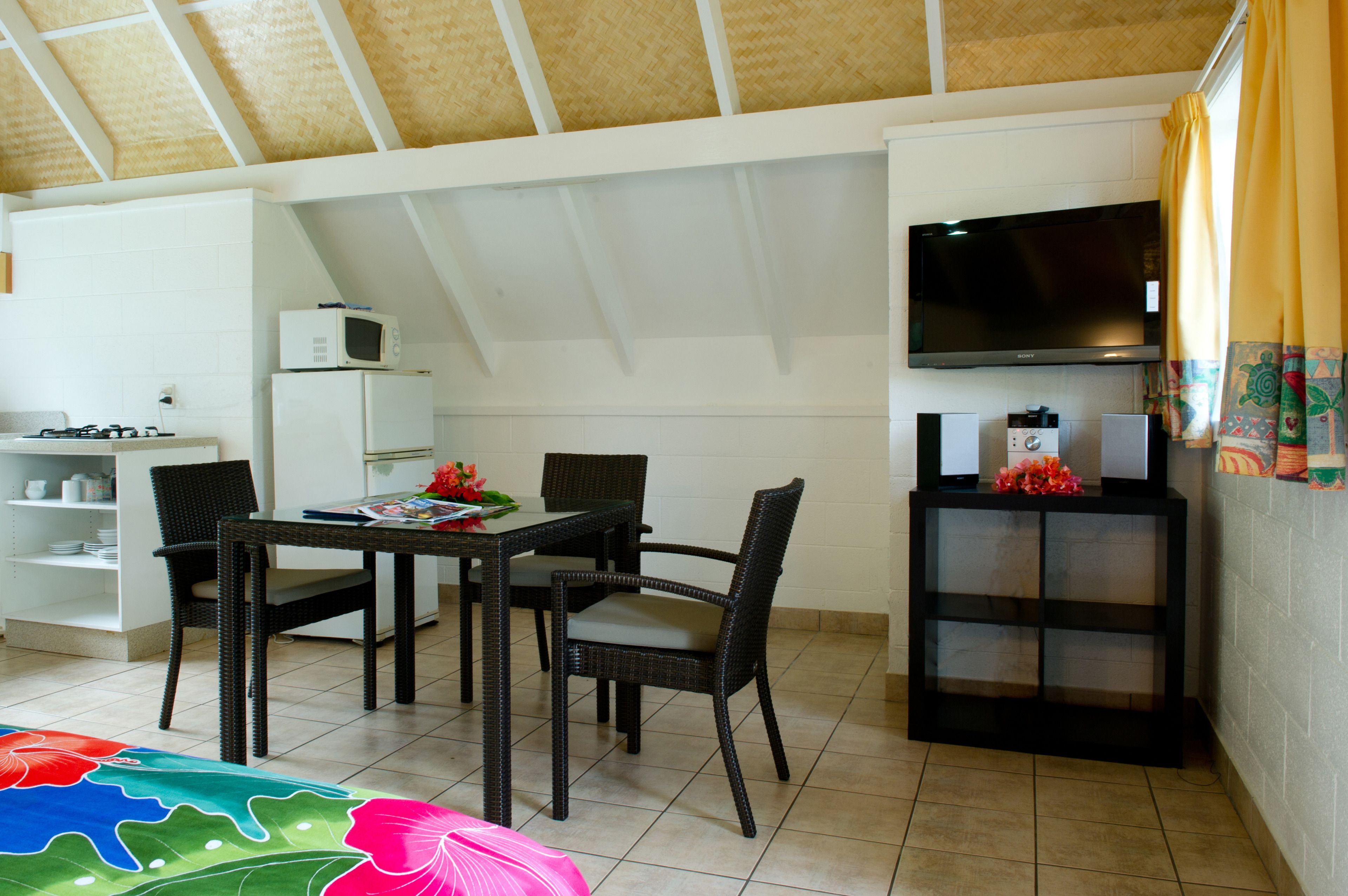 A compact room with a dining table, chairs, a TV, and a small kitchenette.