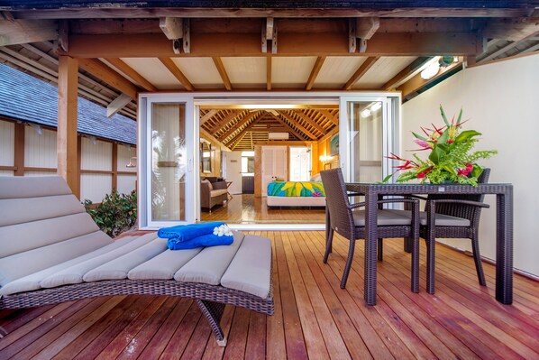 A wooden deck with a wicker lounge chair, a table with chairs, and a potted plant.