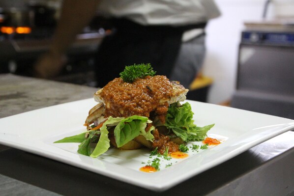 A square plate with a food item, possibly a sandwich, garnished with green leaves and a small sprig of parsley.