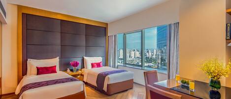 A hotel room with two beds, a dining table, and a view of the city.
