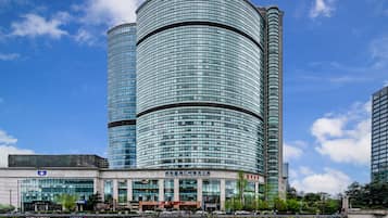 En modern byggnad med en böjd glasfasad, en skylt med texten ”Somerset Riverside Chengdu” och en spegelbild i vattnet.