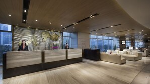 Un área de recepción moderna con un mostrador de madera, una consola negra y un espacio de estar con sofás.