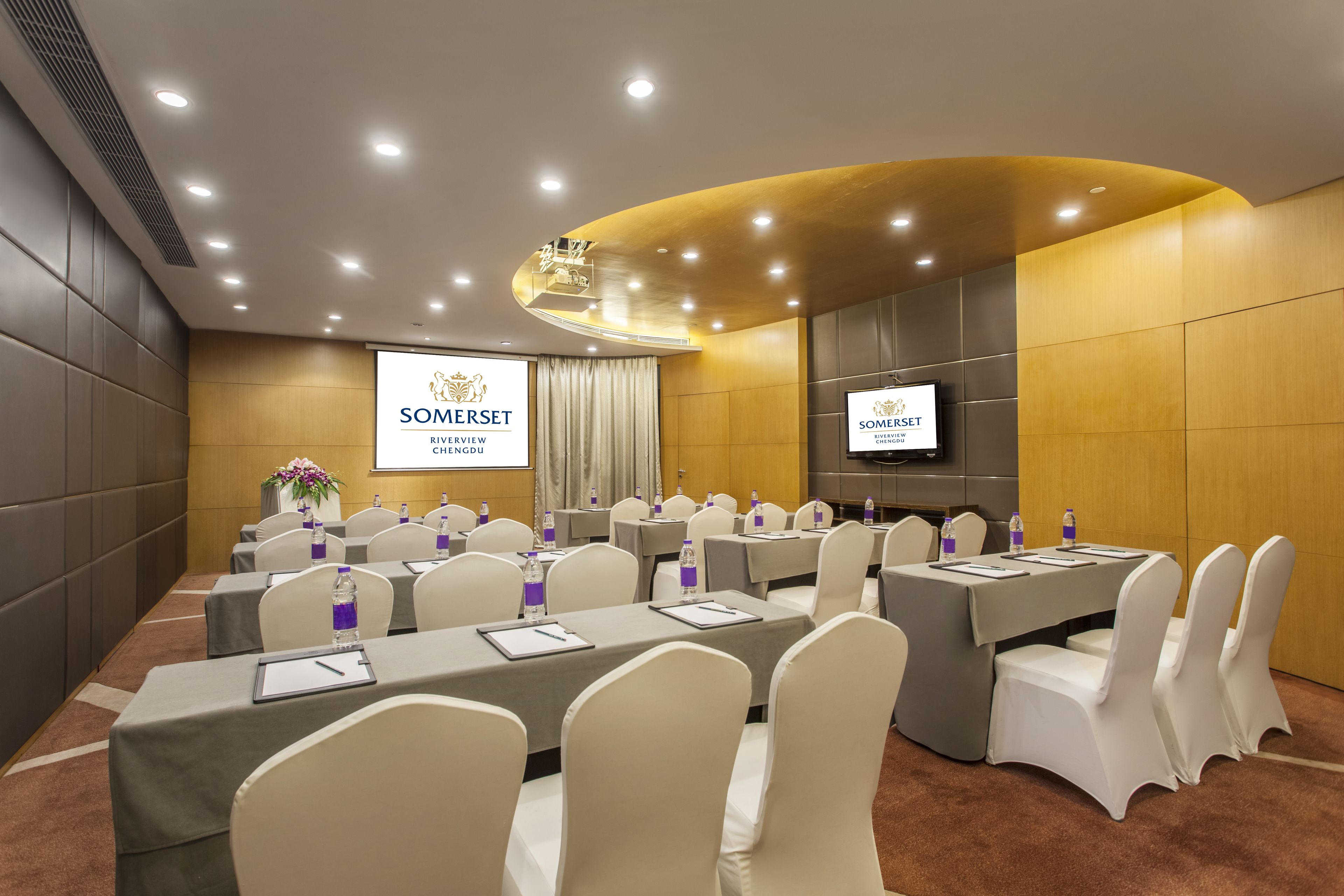 A conference room with multiple tables, chairs, and a large screen displaying the SOMERSET logo.