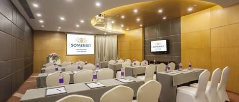 A conference room with multiple tables, chairs, and a large screen displaying the SOMERSET logo.
