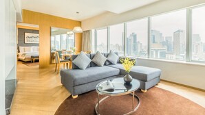 Una sala de estar moderna con un sofá gris, una mesa de centro de vidrio y vistas a un horizonte urbano a través de amplios ventanales.