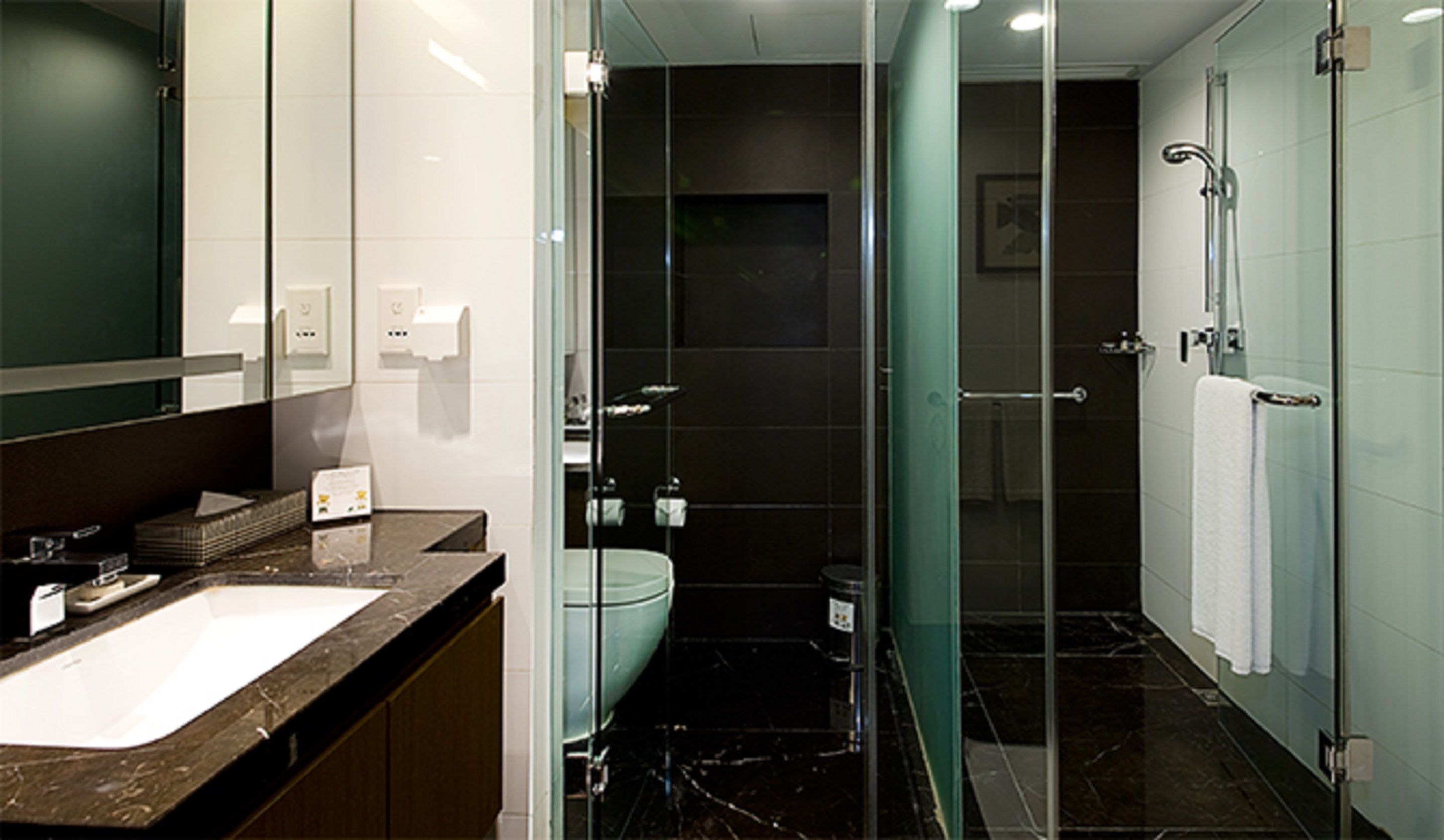 Un baño moderno con lavamanos de mármol, cabina de ducha de vidrio y un inodoro.