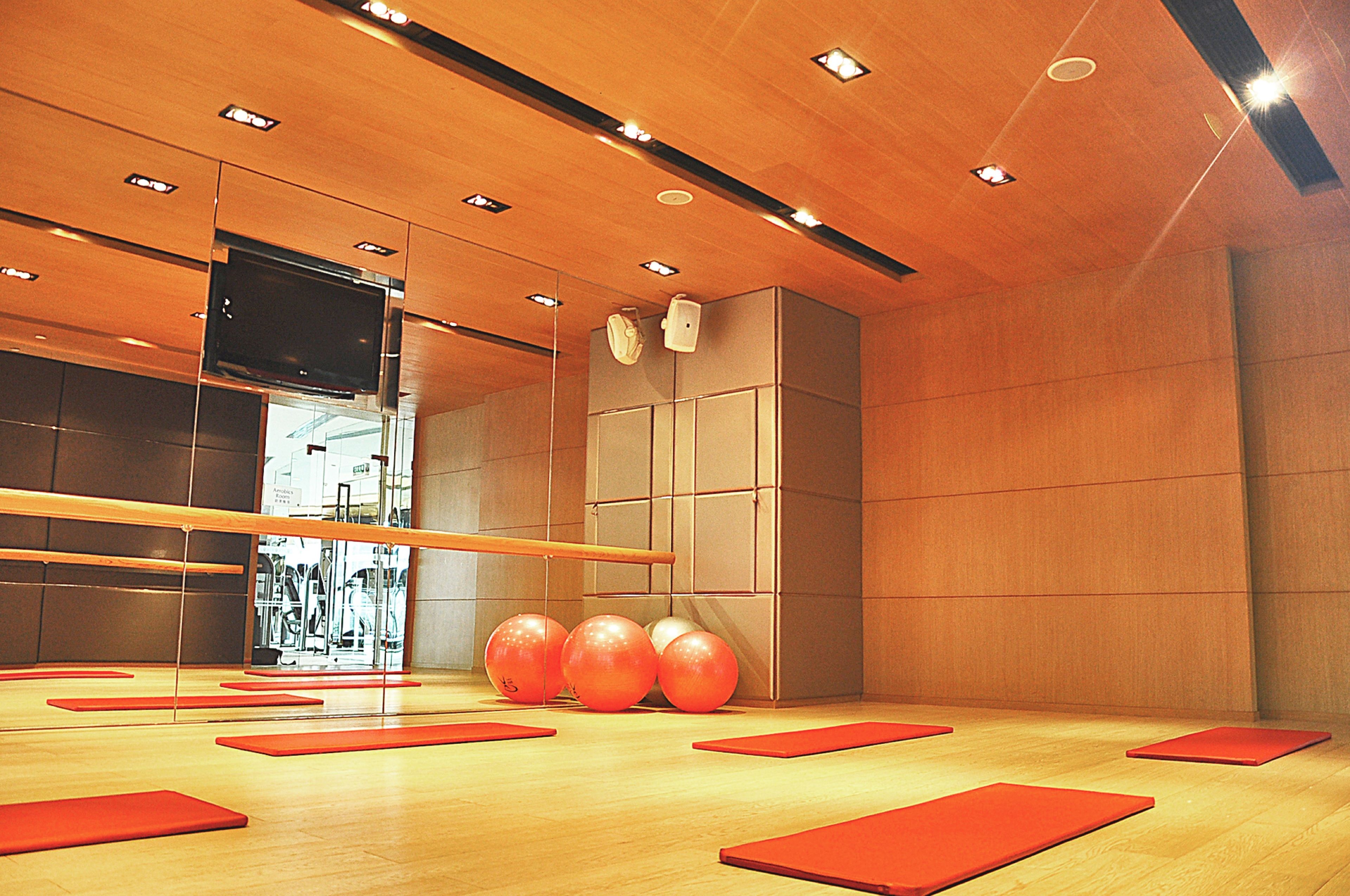Habitación amplia con pisos de madera, un espejo grande y equipo de ejercicio, incluyendo colchonetas rojas y balones de gimnasia.