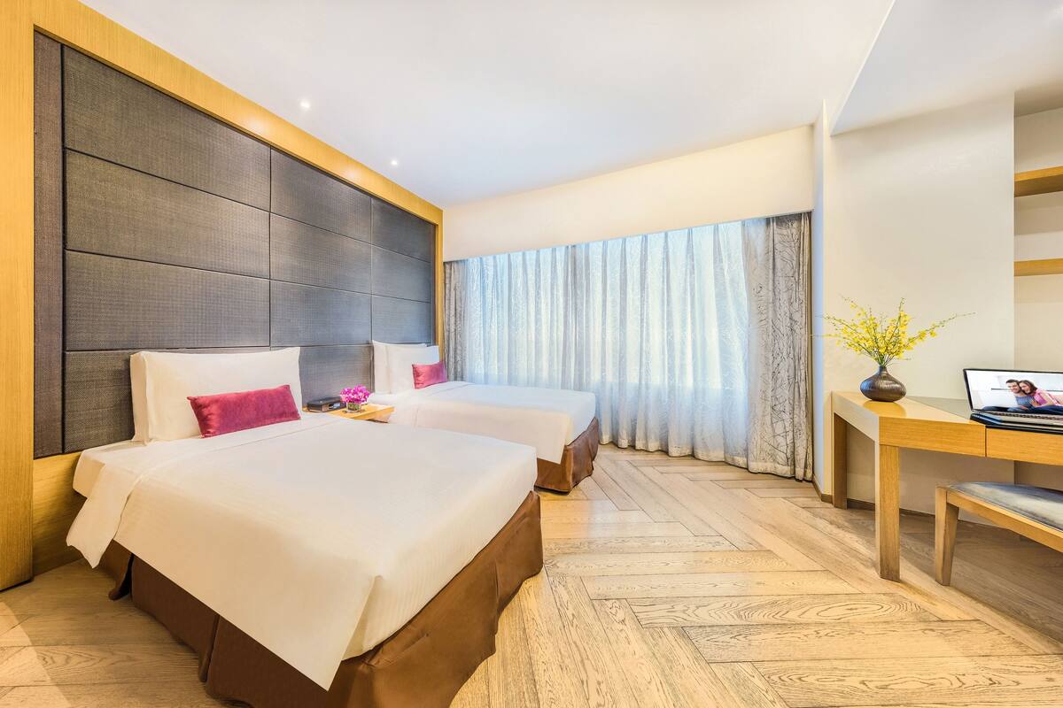 Ett hotellrum med två sängar, ett skrivbord och ett stort fönster med gardiner.