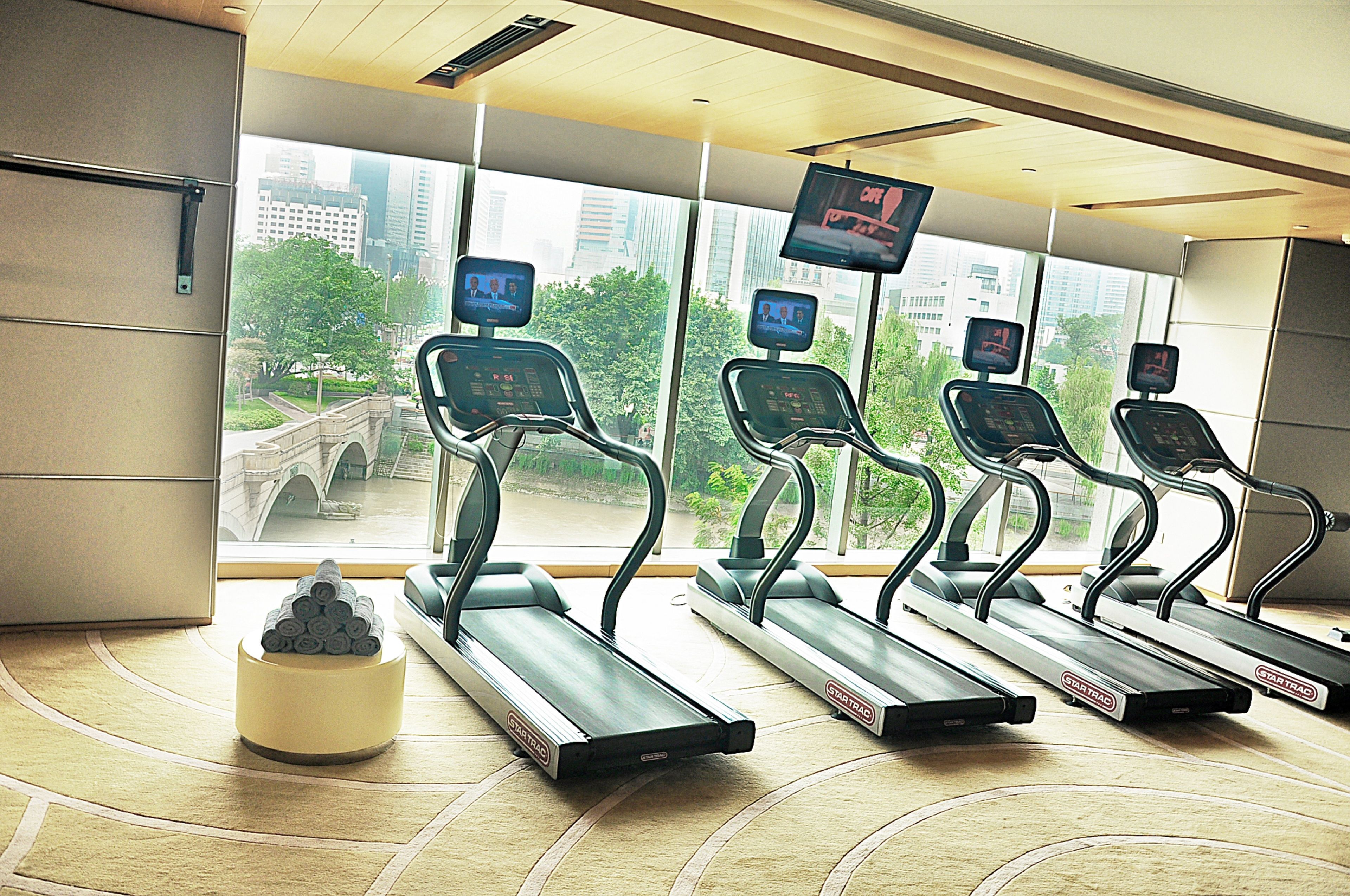 A gym with treadmills, a digital screen, and a view of a cityscape.