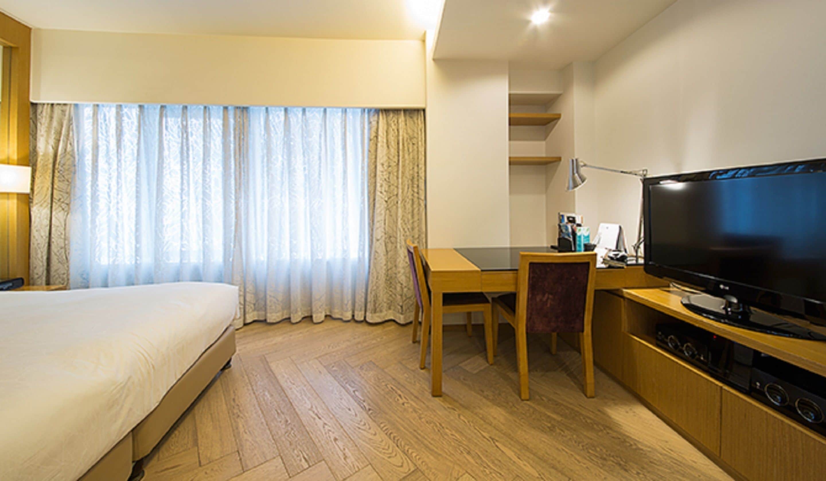 Una habitación de hotel con cama, escritorio con televisor y ventana con cortinas.