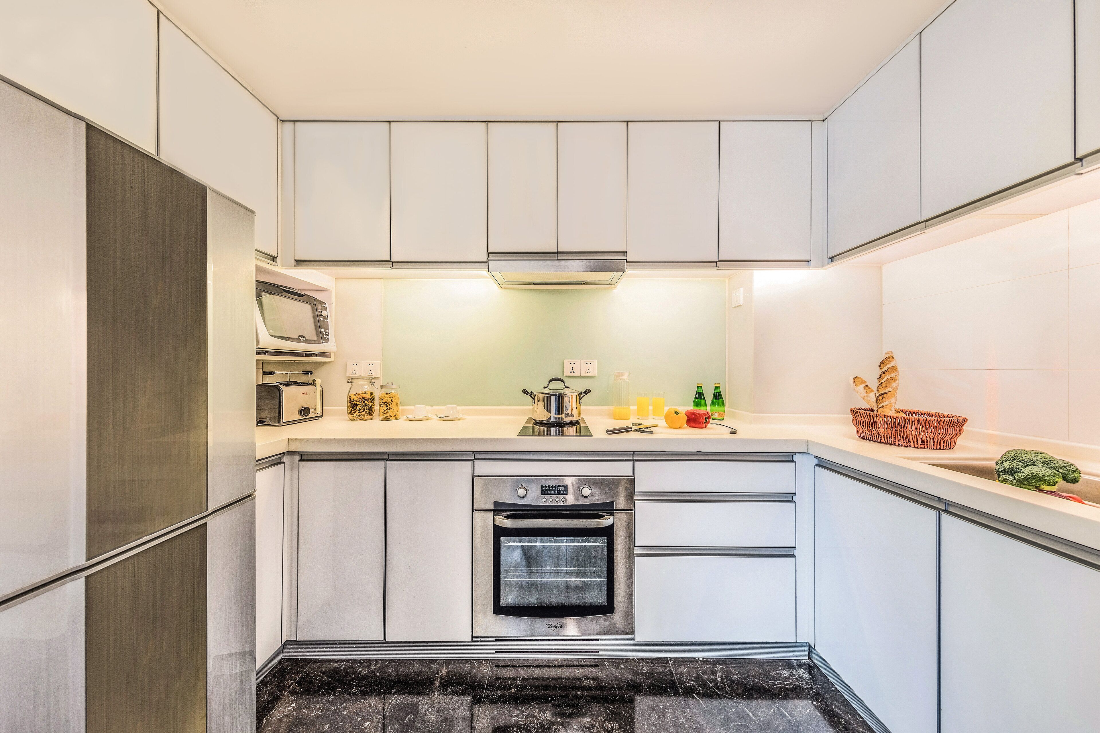 Una cocina moderna con armarios blancos, horno empotrado, microondas y campana extractora de acero inoxidable.
