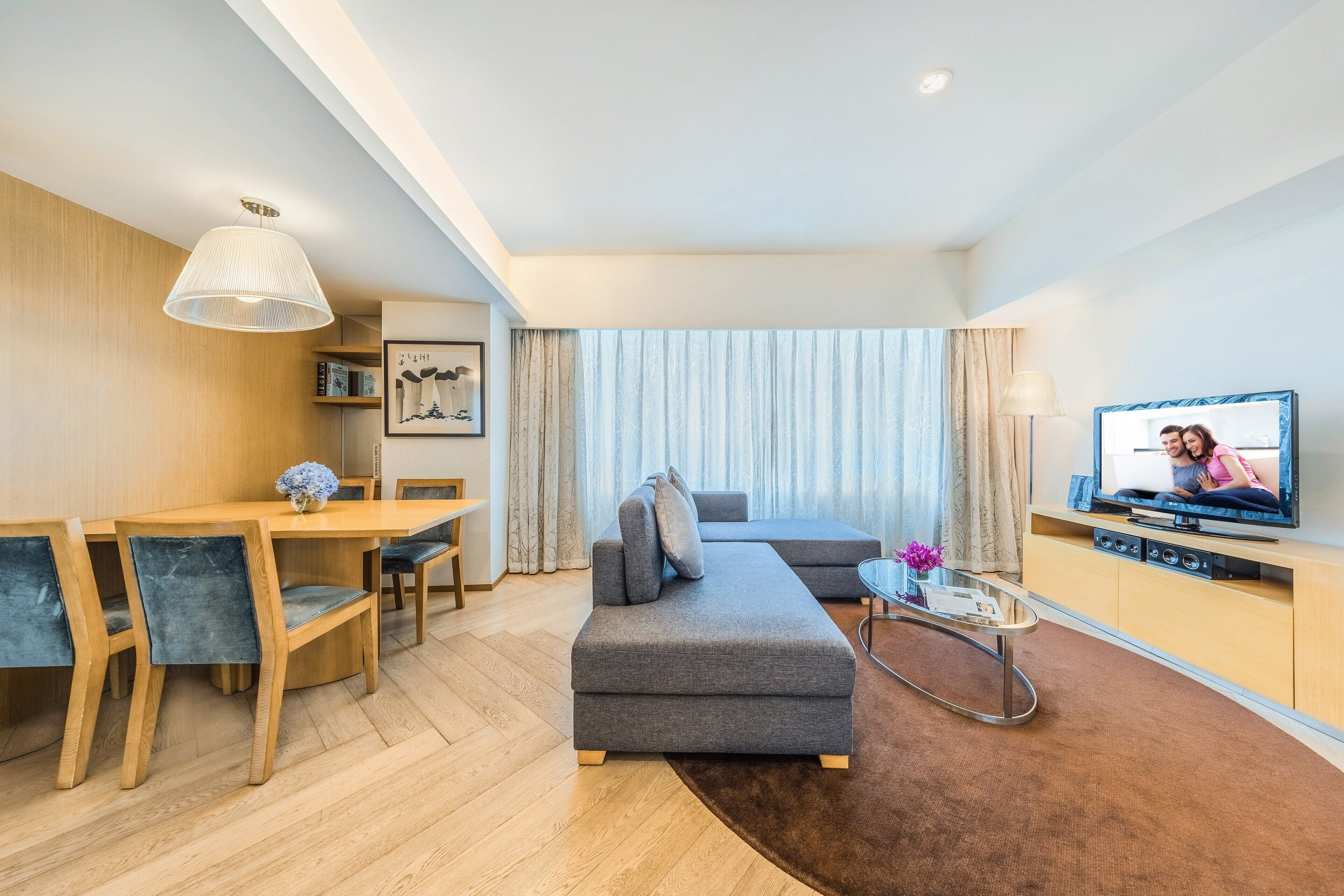 A modern living room with a sofa, TV, dining table, and chairs.