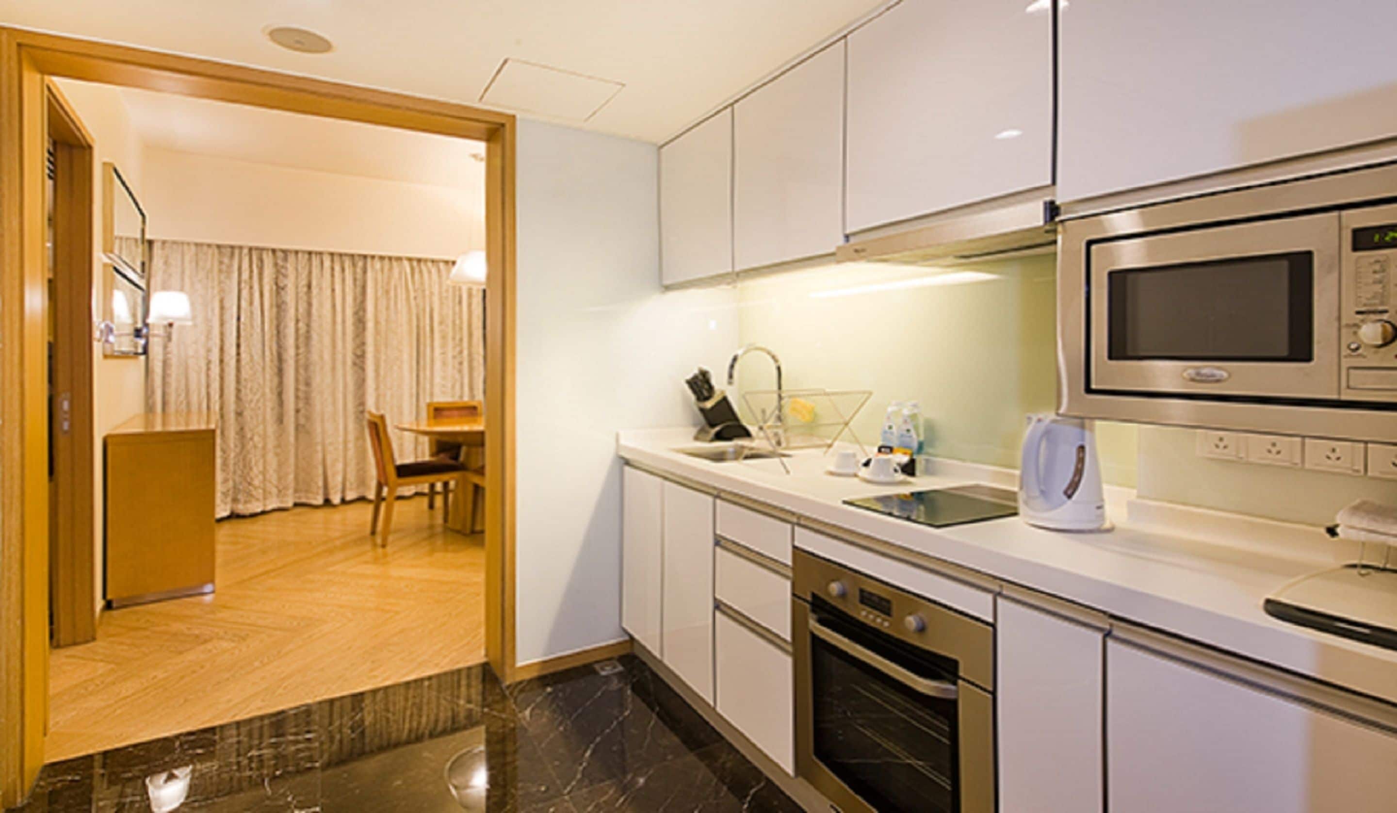 A modern kitchen with a microwave, oven, and sink. There is a dining area with a table and chairs visible through an open door.