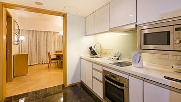 A modern kitchen with a microwave, oven, and sink. There is a dining area with a table and chairs visible through an open door.