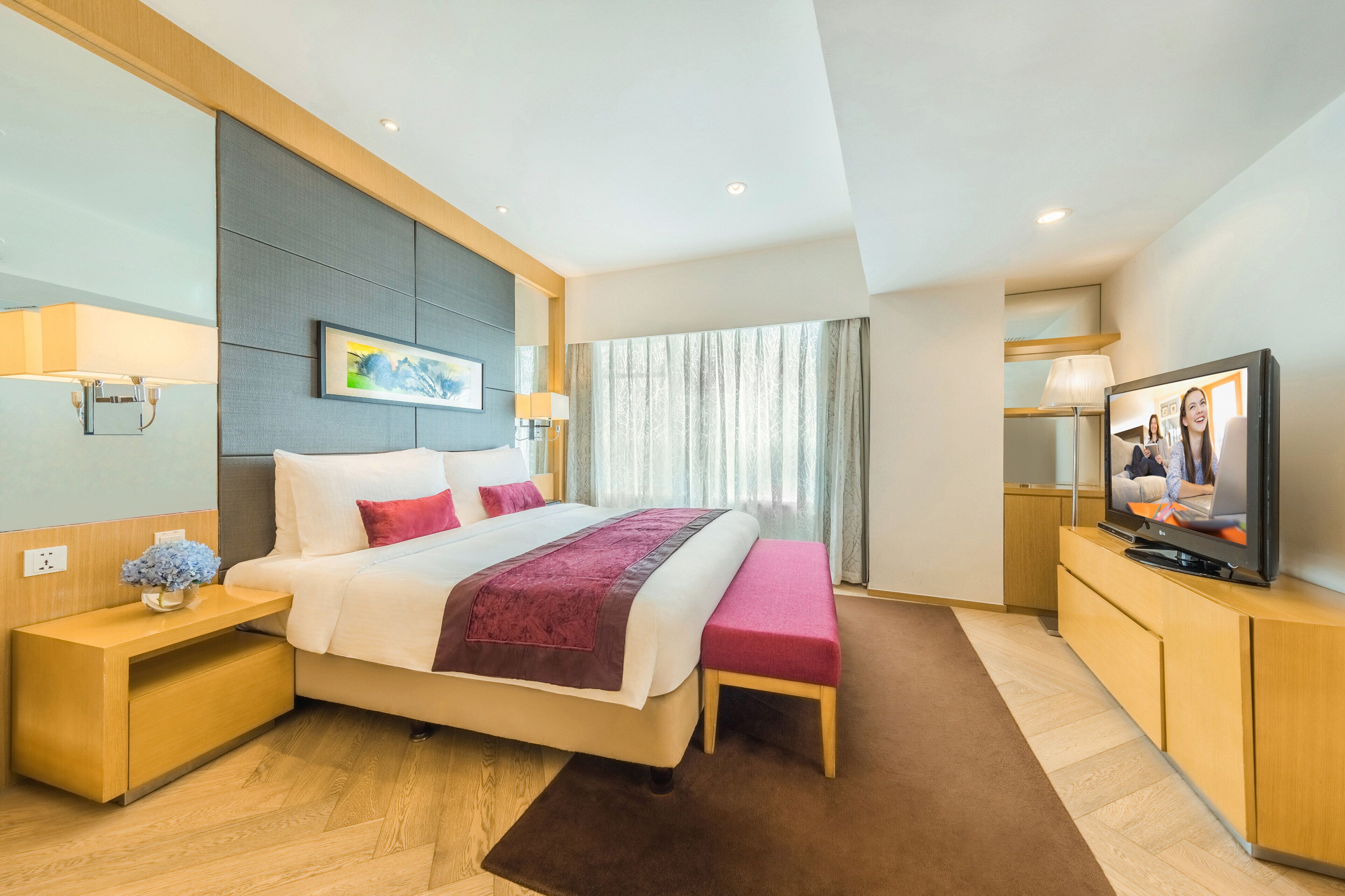 Una habitación de hotel moderna con una cama grande, mesitas de noche, un televisor de pantalla plana y vistas de la ciudad a través de amplios ventanales.