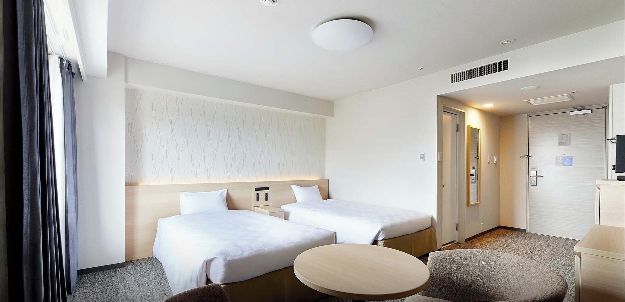 Habitación de hotel con dos camas, una mesa redonda, un sofá, un espejo y una puerta que da a un baño.