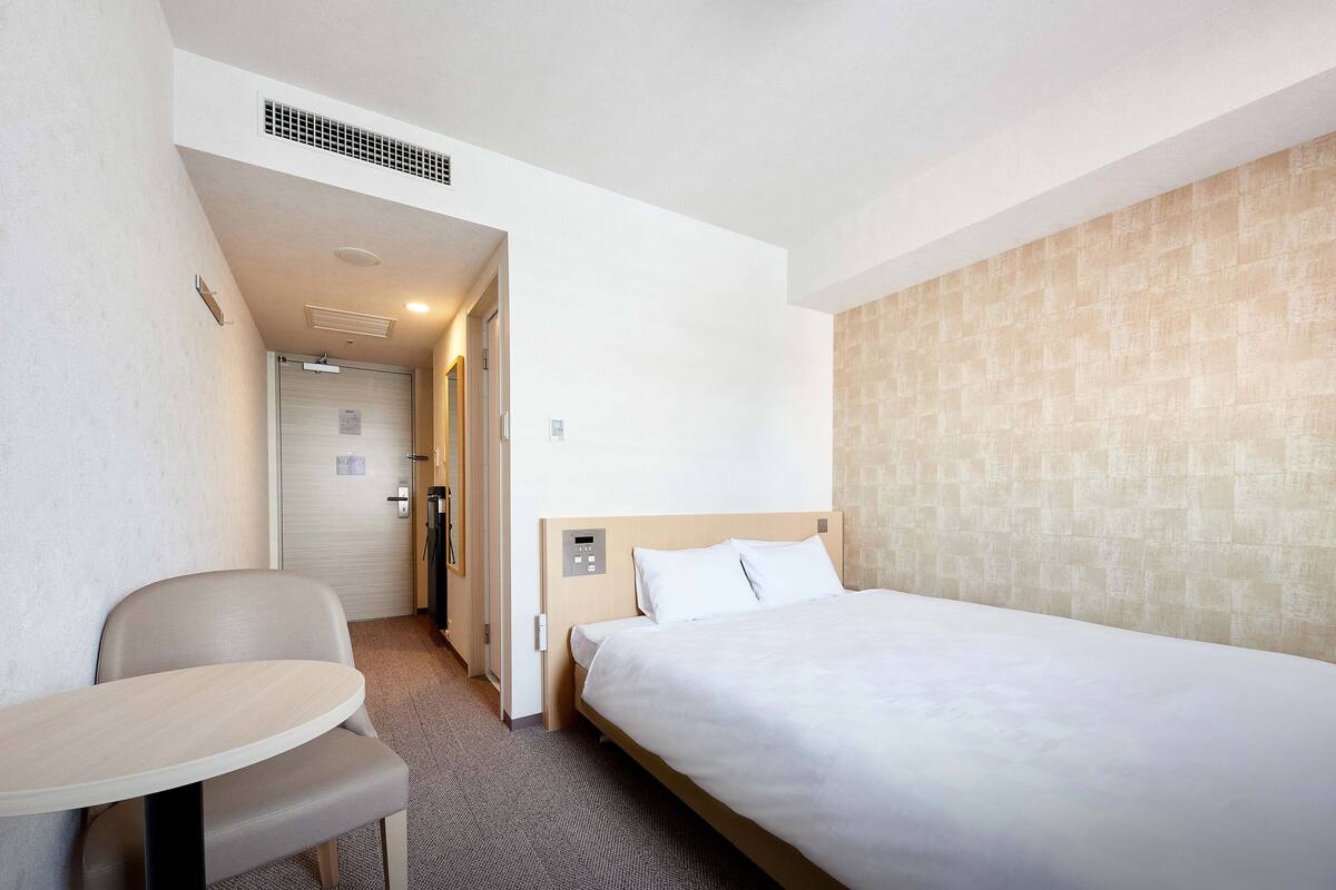 A hotel room with a single bed, a small table, and a chair.