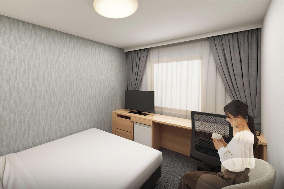 Una habitación de hotel con cama, escritorio, televisor y una silla.