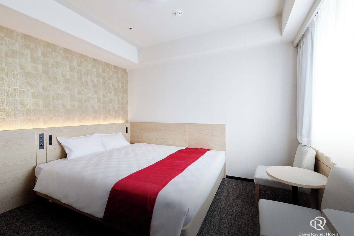 A hotel room with a bed, bedside table, and a small round table.