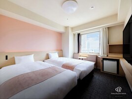 A hotel room with two beds, a small table, a TV, and a window with a city view.