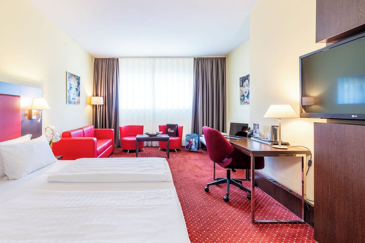 Une chambre d’hôtel avec un grand lit, un bureau, une chaise, une télévision et un canapé rouge.