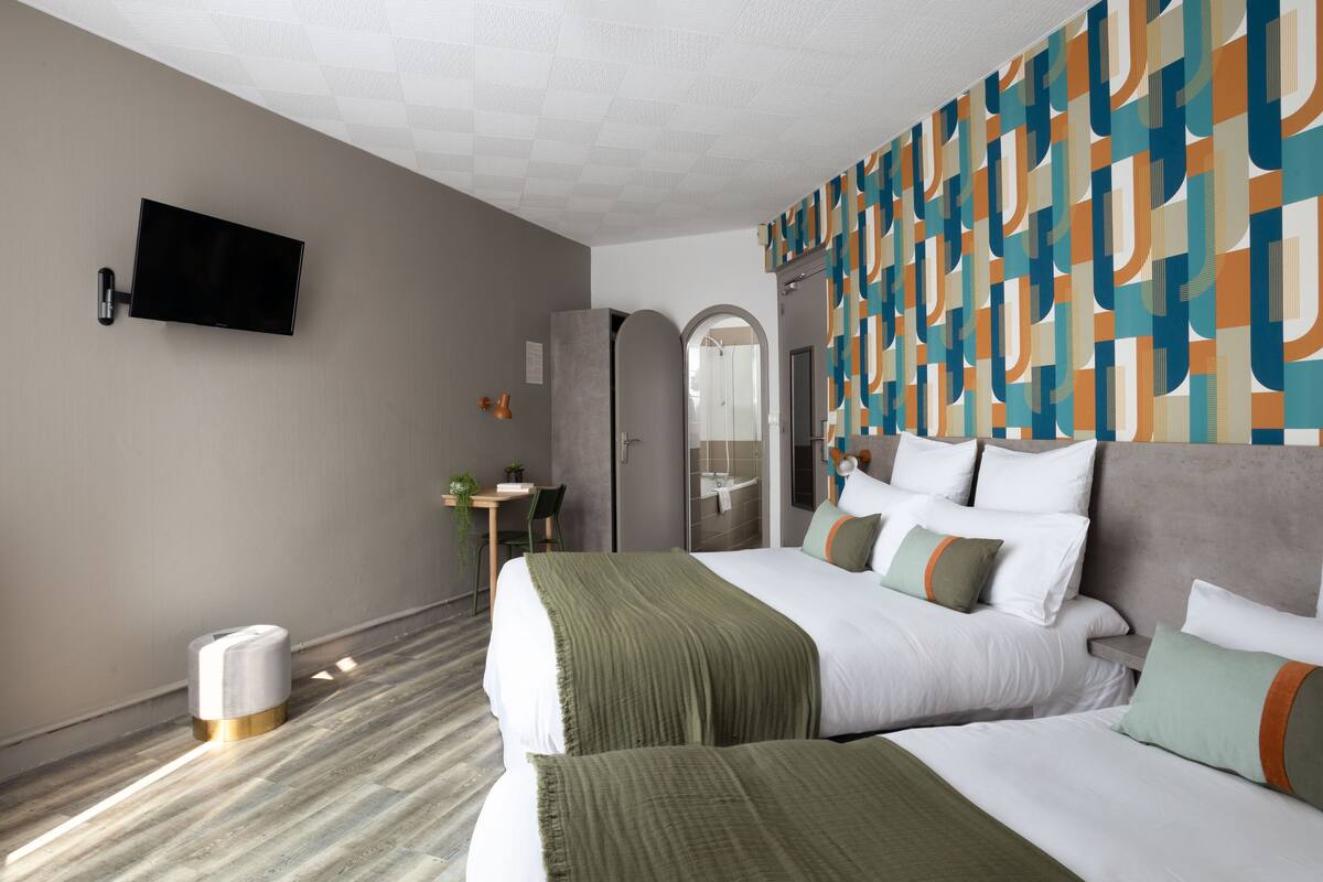 A hotel room with a large bed, a desk with a chair, a television mounted on the wall, and a bathroom with a mirror and shower.