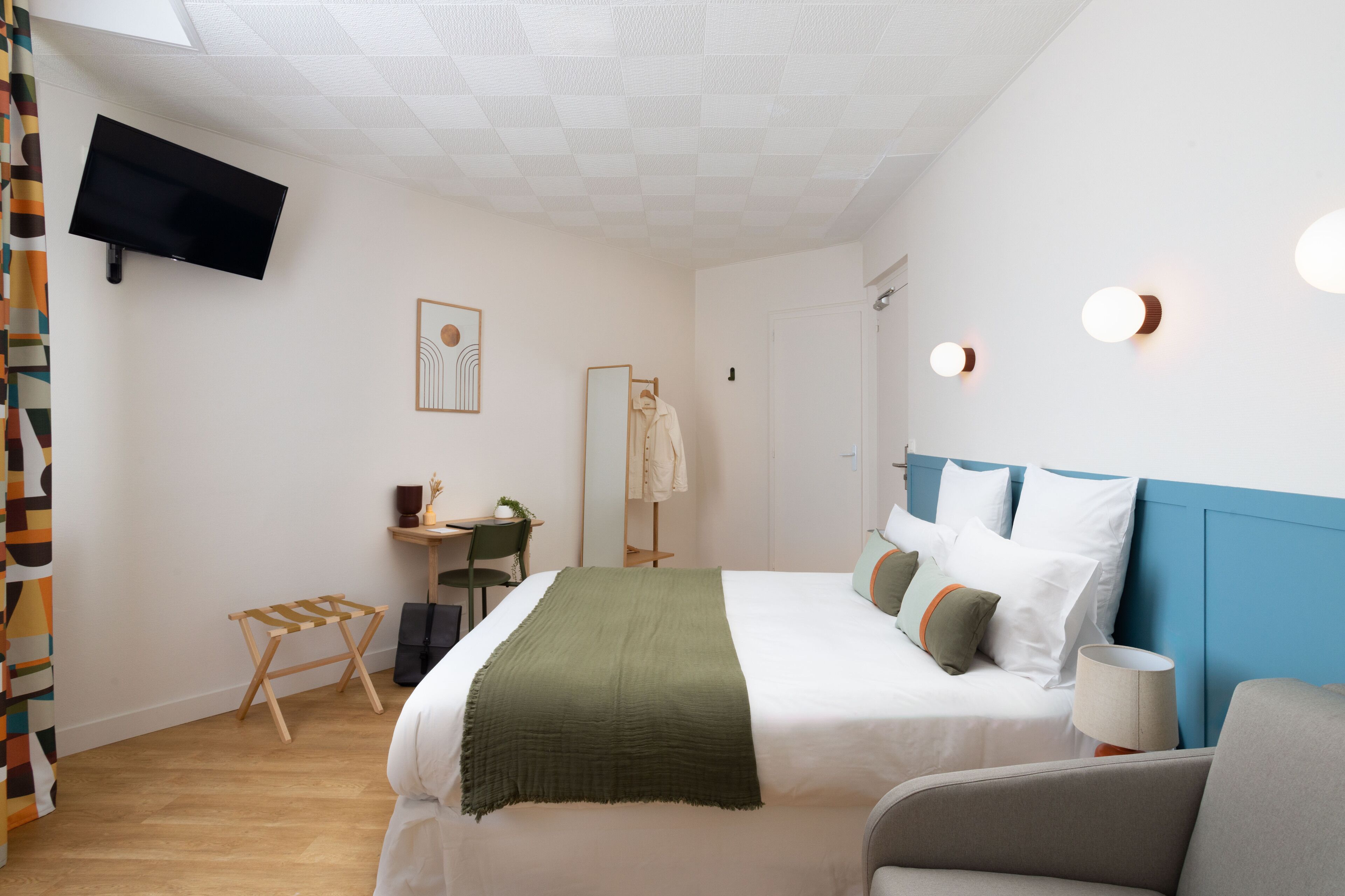 A modern hotel room with a large bed, a desk, a chair, and a television mounted on the wall.