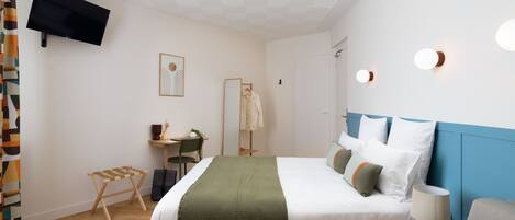 A modern hotel room with a large bed, a desk, a chair, and a television mounted on the wall.