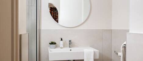 Un baño con un lavamanos blanco, un espejo redondo y una toalla colgada en la pared.