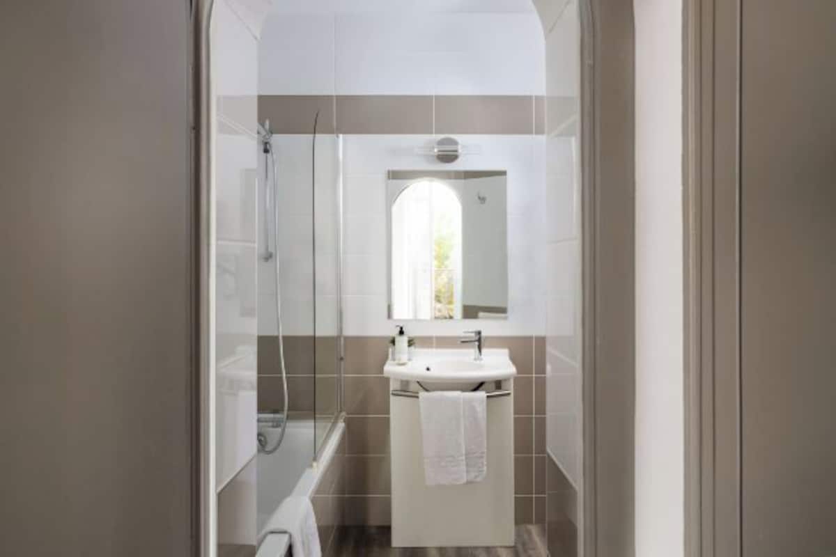 Un baño con ducha de vidrio, un lavamanos blanco con espejo y una toalla colgada en la pared.
