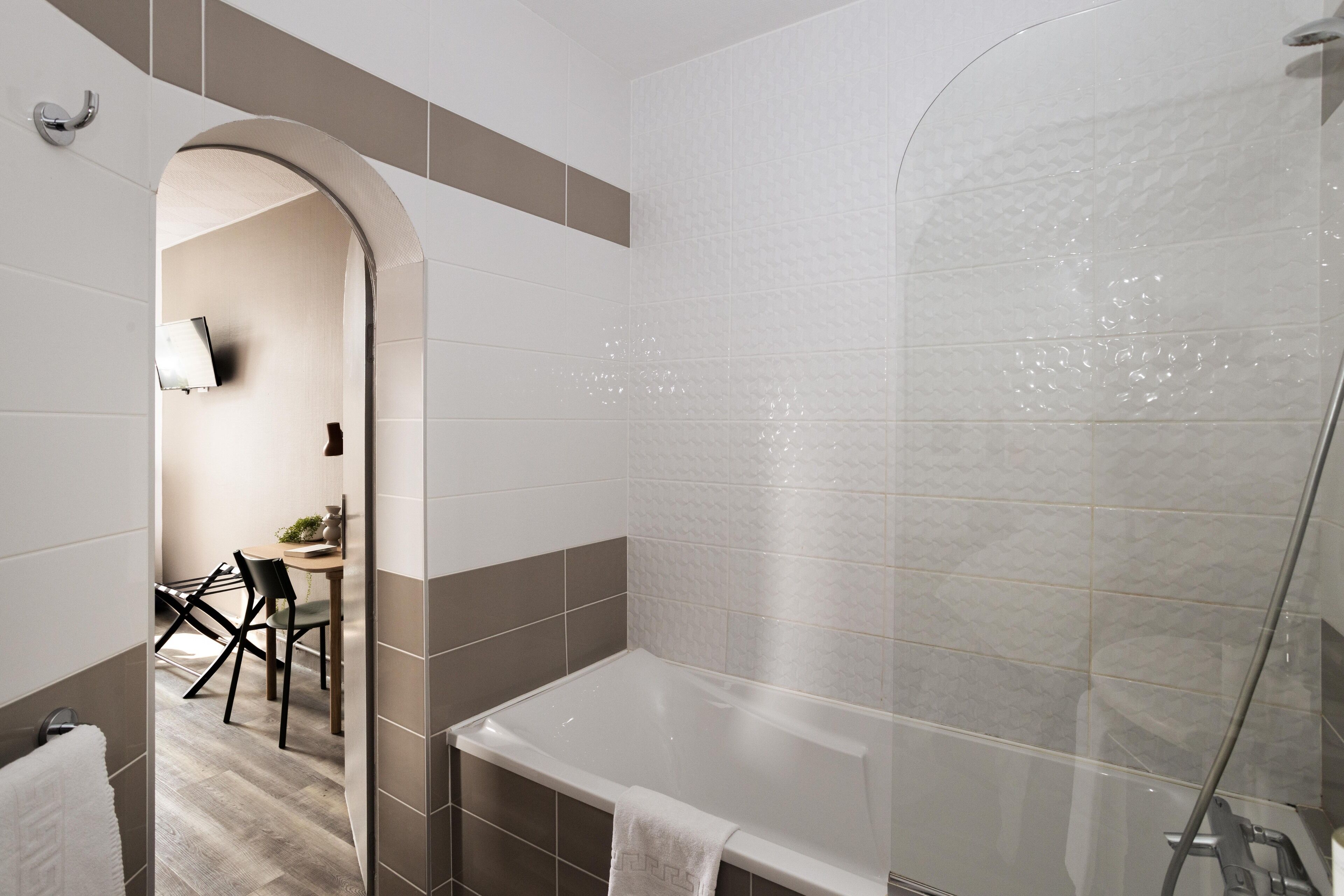 A modern bathroom with a glass shower enclosure, a bathtub, and a seating area with a table and chairs.