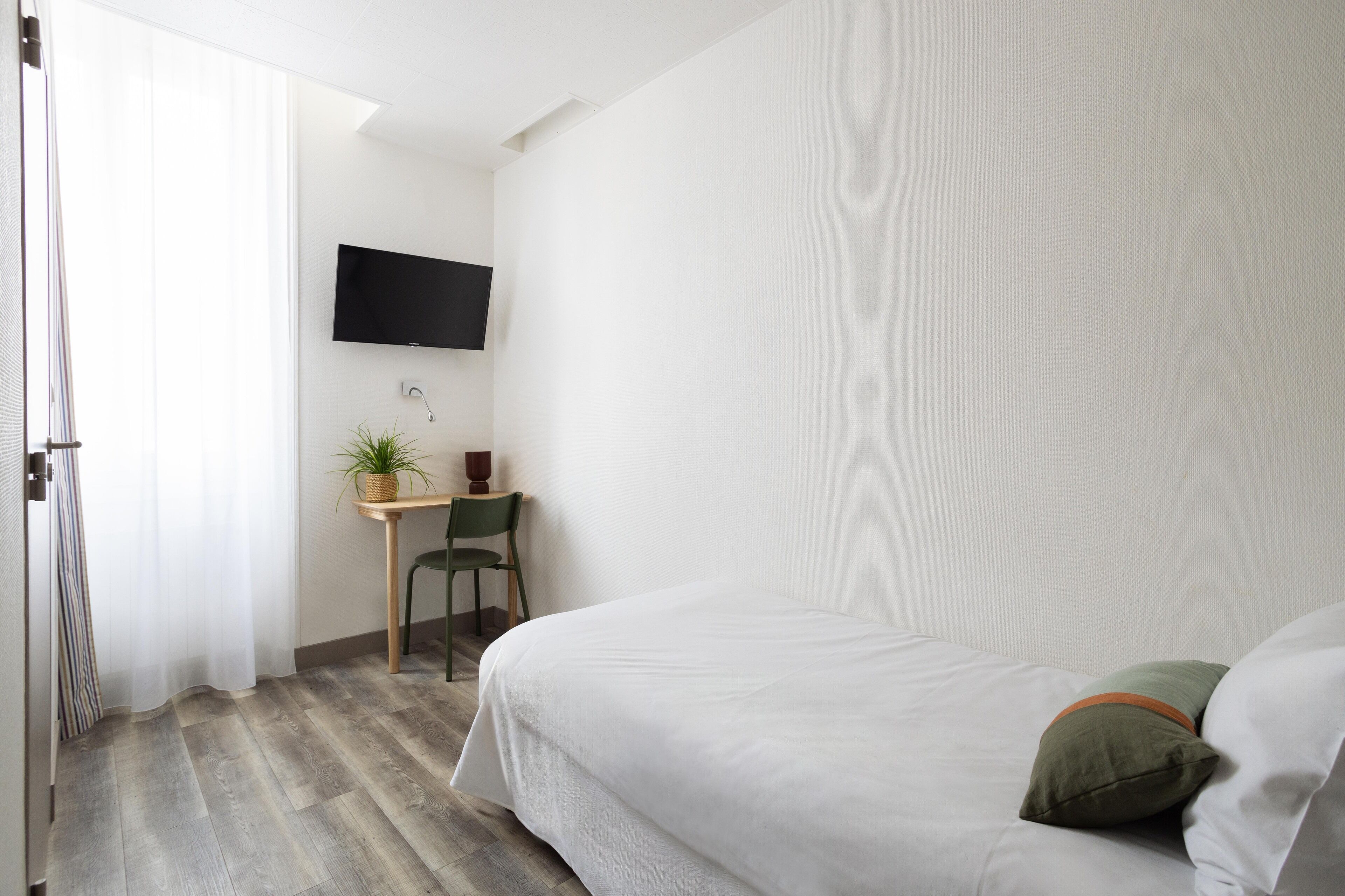 Une chambre à coucher avec un lit, un bureau et une chaise, une télévision et une plante en pot.