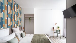 A modern hotel room with a large bed, a desk, and a television.