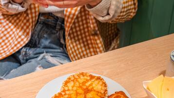 A person holding a cup with a frothy beverage, a plate with croissants and a honey dipper, and a bowl of granola.