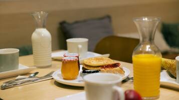 A breakfast table with plates of food, a glass of orange juice, and a bottle of milk.