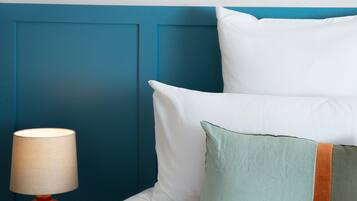 A neatly made bed with white and green pillows, a teal headboard, and a red lamp on a white nightstand.