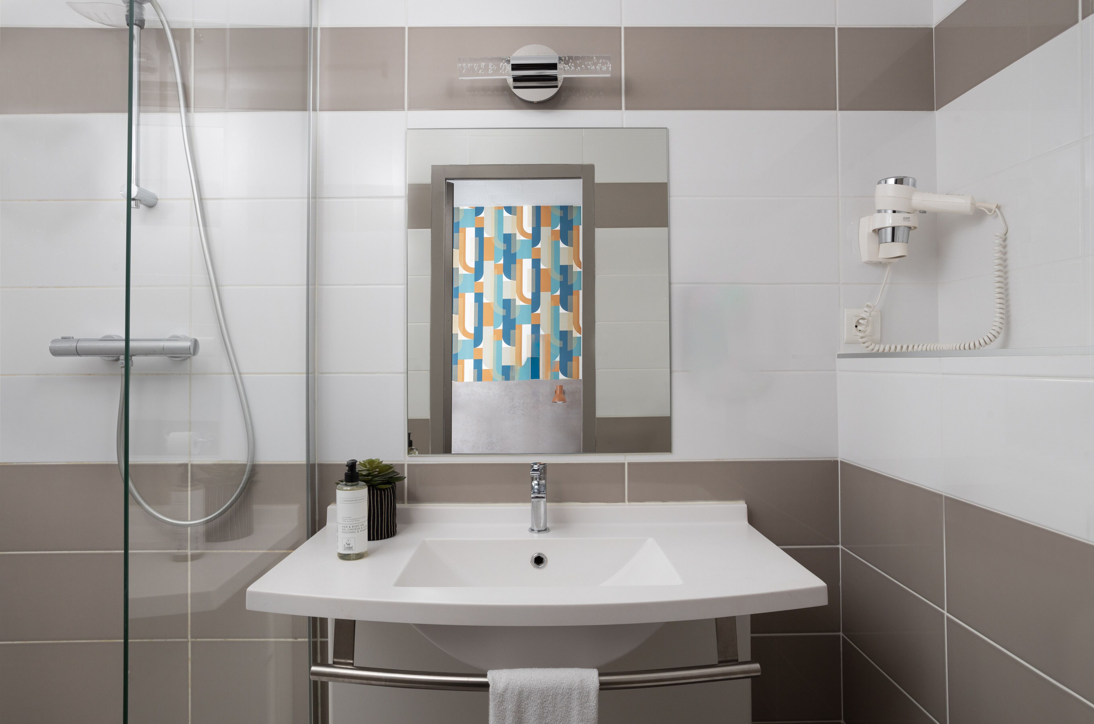 A modern bathroom with a glass-enclosed shower, a white sink with a mirror above it, and a towel hanging on a metal rack.