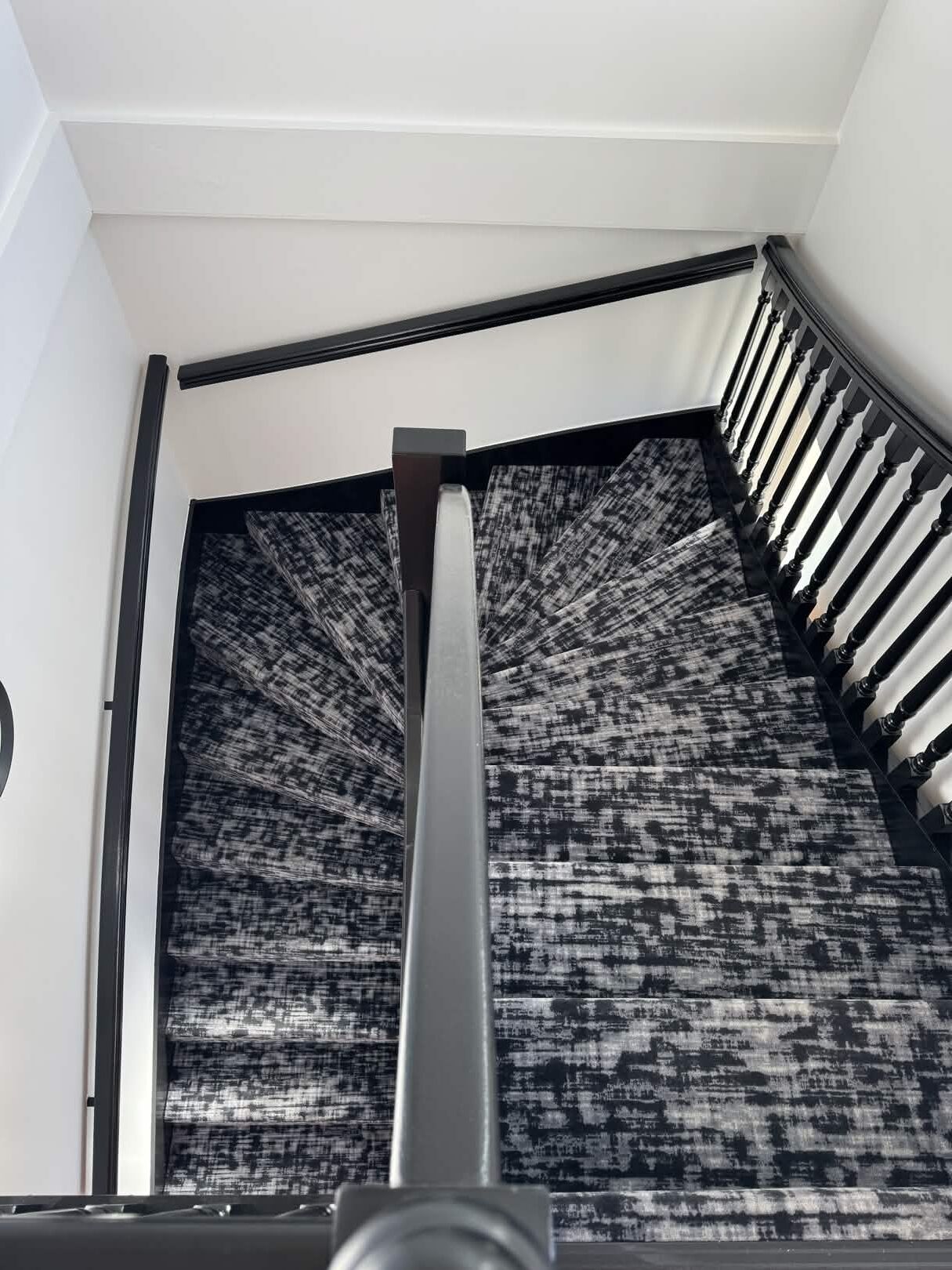 Un escalier avec une rampe noire et un mur orné de motifs.